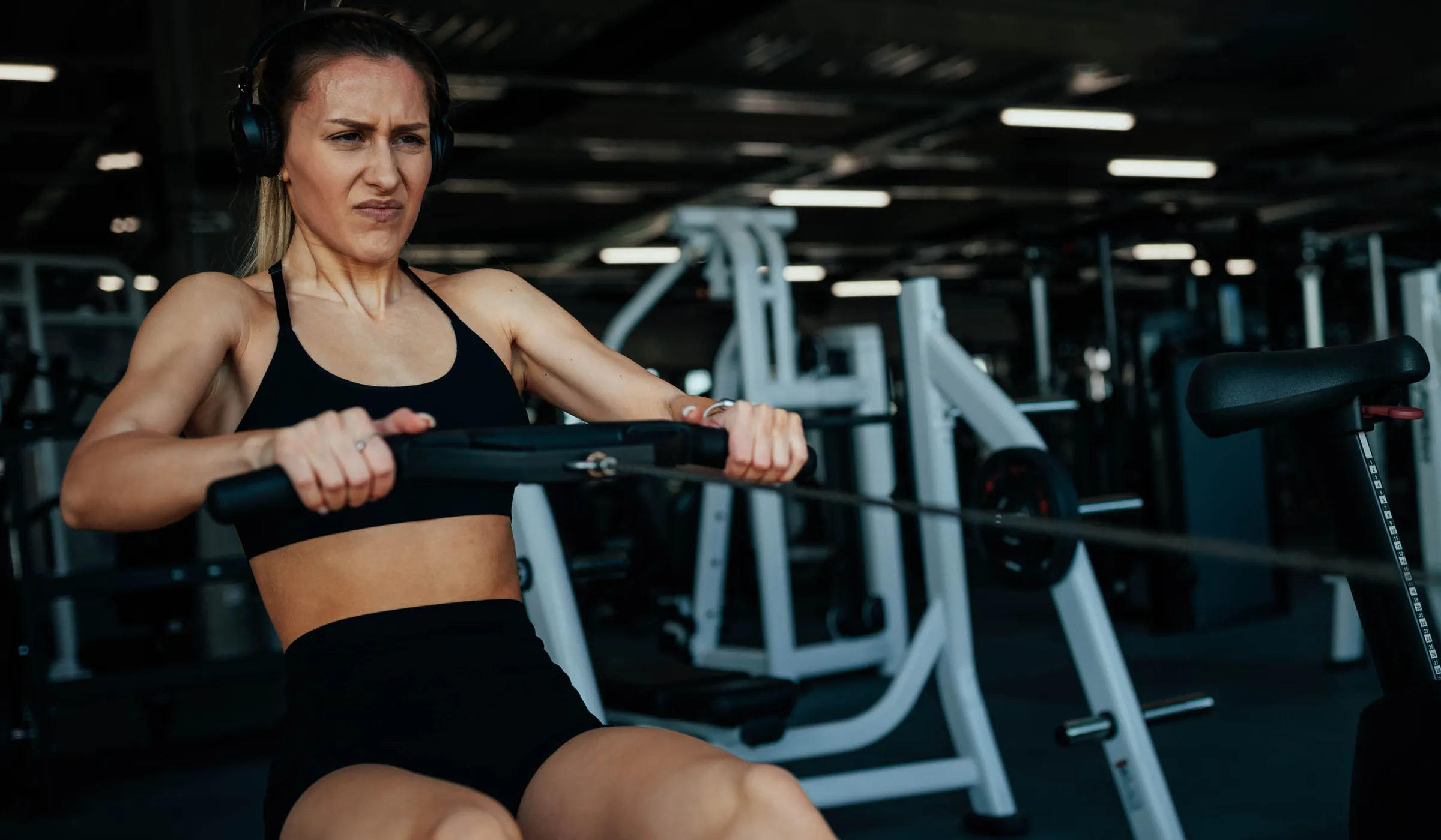 Sportlerin trainiert in einem Fitnessstudio an einem Rudergerät; oben rechts stehen die Logos von BIG direkt gesund und HYROX als offizieller Gesundheitspartner Dach