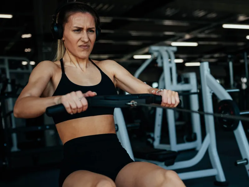 Sportlerin trainiert in einem Fitnessstudio an einem Rudergerät; oben rechts stehen die Logos von BIG direkt gesund und HYROX als offizieller Gesundheitspartner Dach